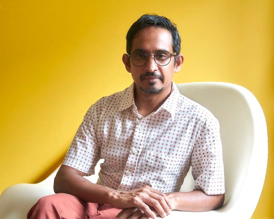 Photo of author seated in an ivory womb-chair against a yellow background